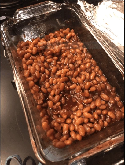 A bowl of perfectly baked beans garnished with fresh parsley, served on a rustic wooden table, showcasing their rich, glossy texture