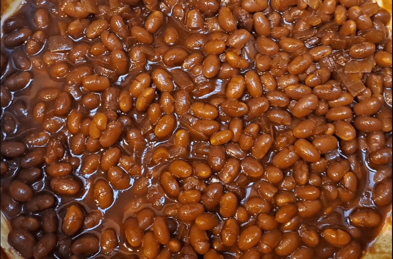 A bowl of perfectly baked beans garnished with fresh parsley, served on a rustic wooden table, showcasing their rich, glossy texture