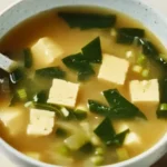 Homemade miso soup in a ceramic bowl featuring silken tofu, seaweed, and scallions in a rich umami dashi broth