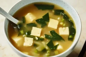 Homemade miso soup in a ceramic bowl featuring silken tofu, seaweed, and scallions in a rich umami dashi broth
