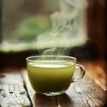 Close-up of a steaming glass cup of Japanese Mounjaro tea with vibrant green matcha color on a rustic wooden table.