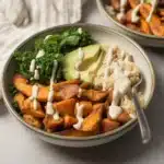 Delicious chicken sweet potato bowl topped with roasted veggies and chipotle sauce.