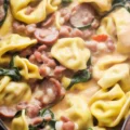 Bowl of Crockpot Cheese Tortellini and Sausage with spinach and tomatoes.