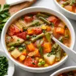 A bowl of healthy vegetable soup topped with fresh herbs and colorful veggies