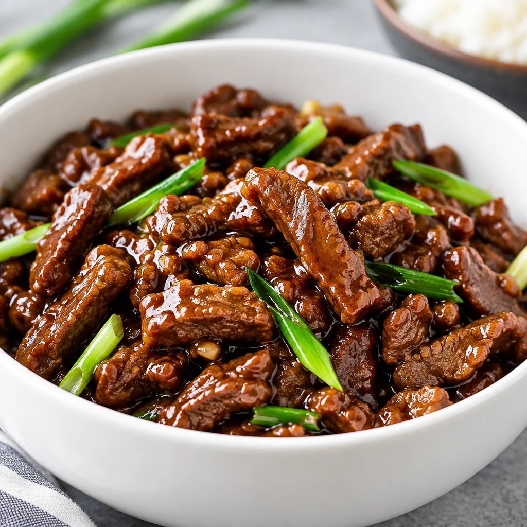 Slow cooker Mongolian beef cooked with garlic, ginger, and soy sauce, served over rice.